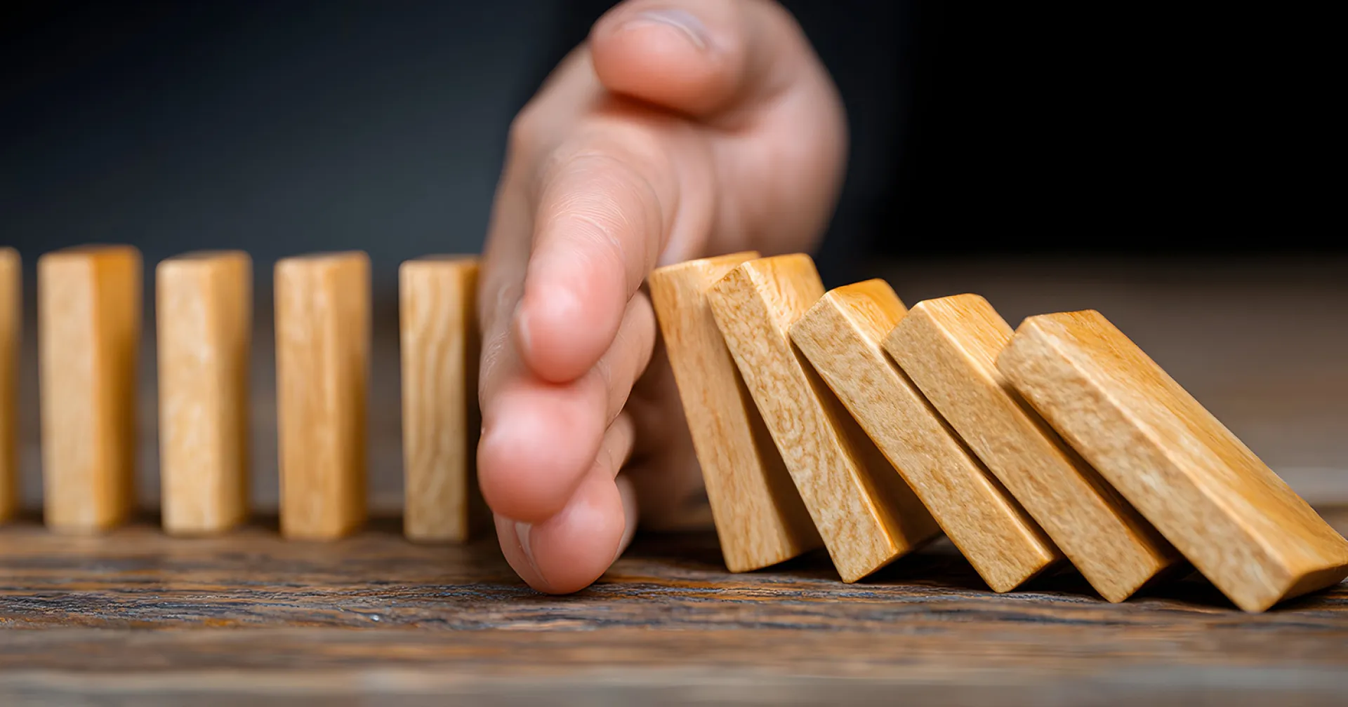 Een hand voorkomt een keting reactie van houten domino steentjes