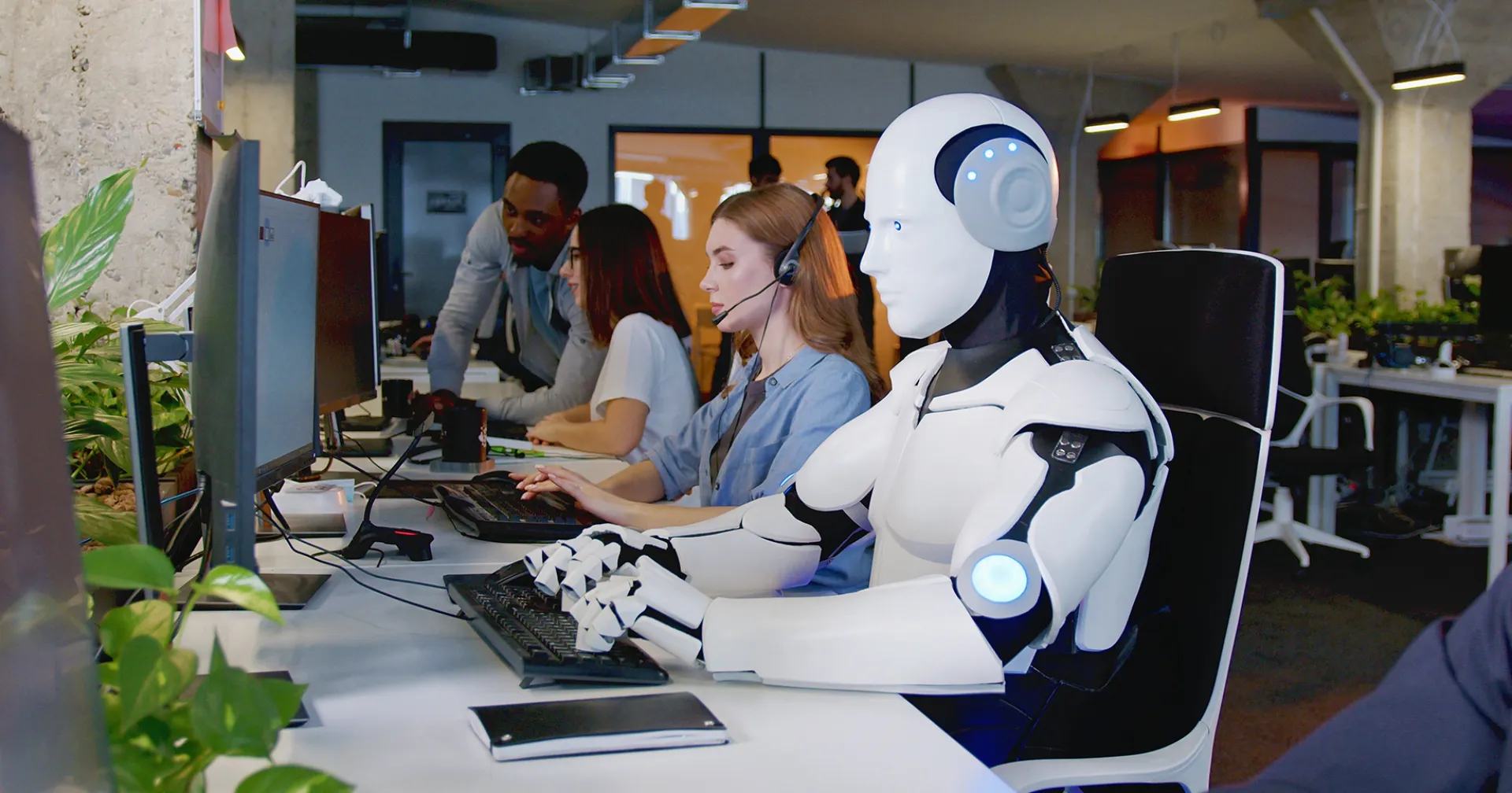 In een ebdrijf zit een robot achter de computer naast mensen