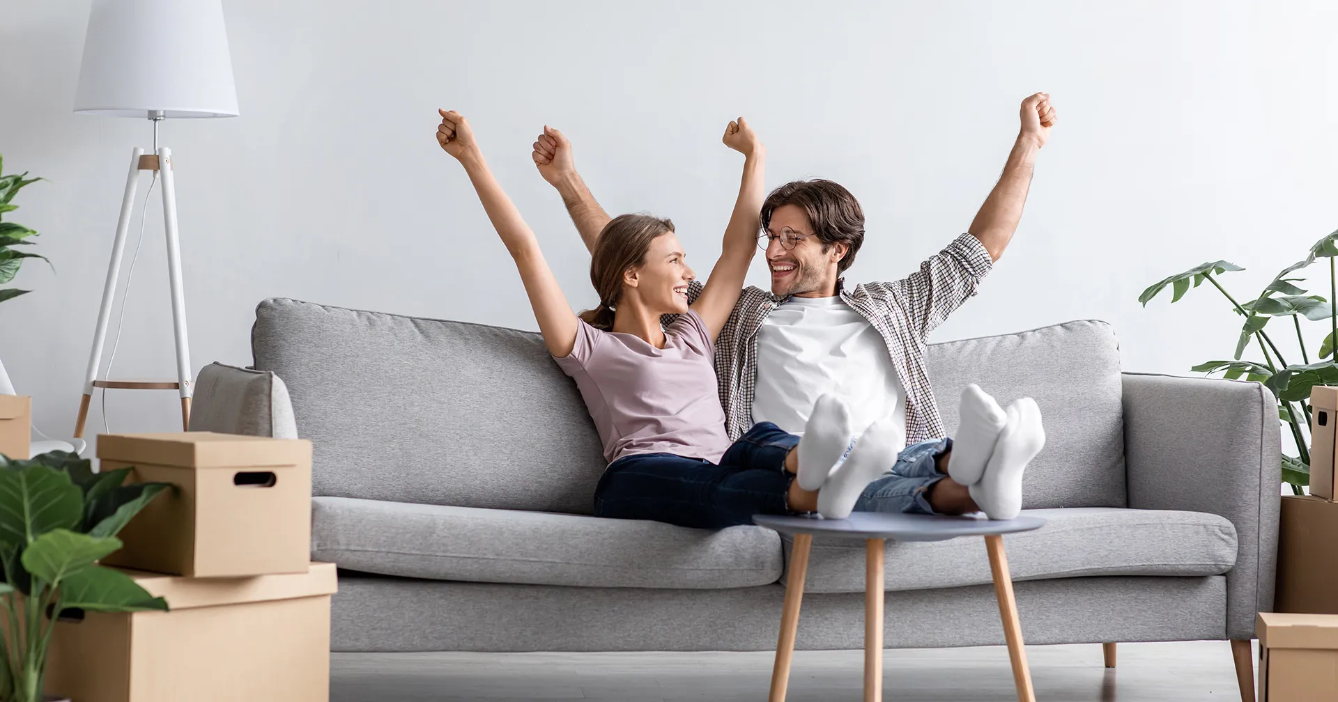 Jong stel dat samen is gaan wonen en op de bank zit met de armen omhoog van blijdschap